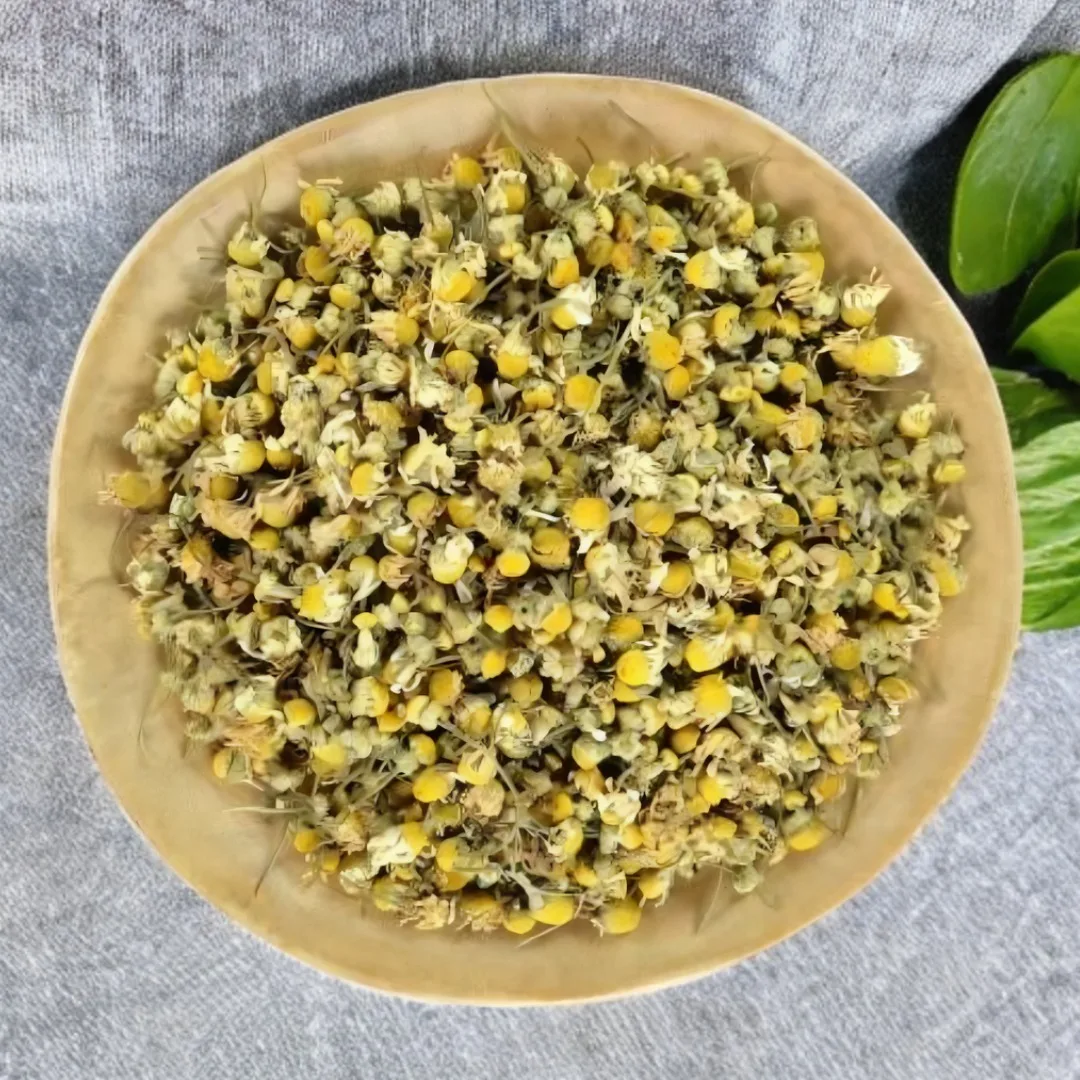 Chamomile Flower Tea – Caffeine-Free Infusion 1 Bowl of dried chamomile flowers with green leaves on fabric surface
